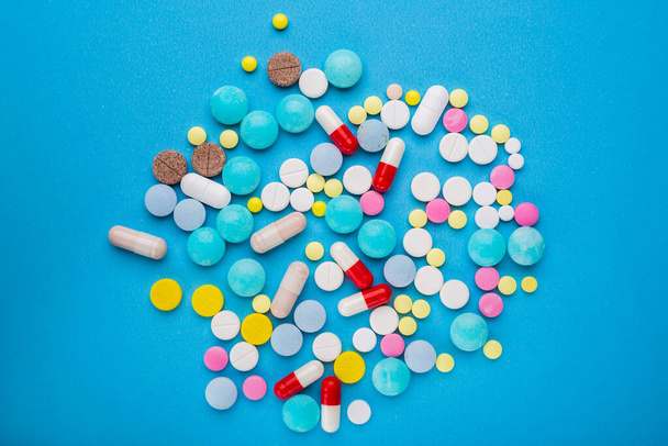 Um monte de comprimidos multicoloridos e cápsulas em um fundo azul como um conceito de dependência da medicina.  - Foto, Imagem