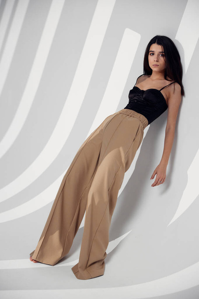 romantic woman in beige pants leaning against the wall brunette model black top - Photo, image