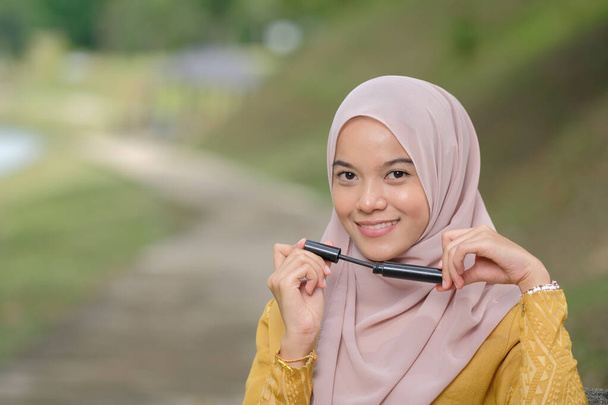 Mooi hijab meisje met mascara over groene achtergrond. Schoonheidsproduct scheut concept. - Foto, afbeelding