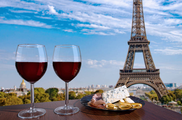 Dvě sklenice červeného vína s občerstvením s výhledem na Paříž a Eiffelovu věž. Sklenice červeného vína s různými občerstveními - talíř se šunkou, plátky, modrý sýr. Pár romantických oslav. Kavárna s výhledem. - Fotografie, Obrázek