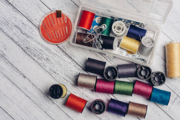 gekleurde draden in een verspreide positie op een houten tafel en naalden voor naaiaccessoires - Foto, afbeelding