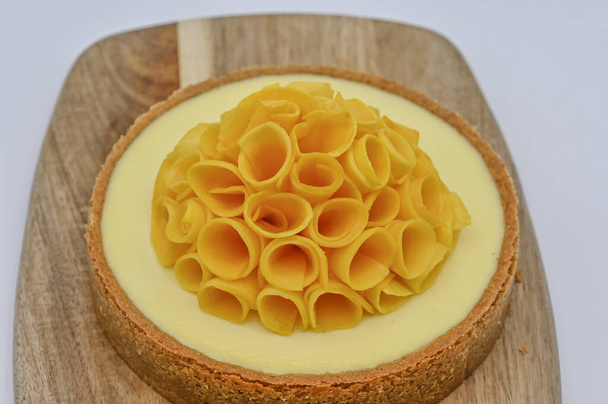 Сырный торт с манго на деревянной доске, украшенной нарезанным свежим манго - Фото, изображение