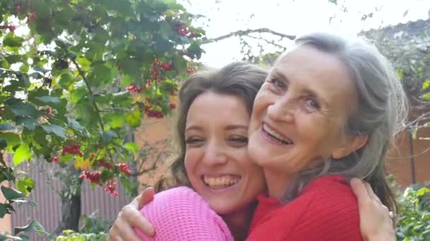 Starší matka s šedivými vlasy se svou dospělou dcerou se objímají během slunečného dne venku na zahradě - Záběry, video