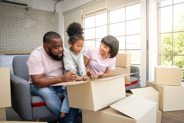 African American family moves to new home Help unpack the paper box. They are happy. The daughter looked at the cardboard box, the father and mother smiled at her. Concept of mixed race family - Photo, Image