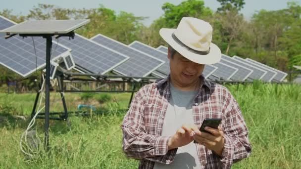 アジアの農家は、スマートフォンを使って太陽電池の温度を調整し、太陽電池の雨やほこりや汚れの後に太陽電池の性能を確認しています。農業技術の概念。スローモーションで撃たれた. - 映像、動画