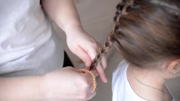 Mutter Frau macht die Frisur ihrer Tochter zu einem kaukasischen Mädchen zu Hause. Selbstversorgung authentisches Konzept. Flechten der Haare auf dem Kopf. - Filmmaterial, Video