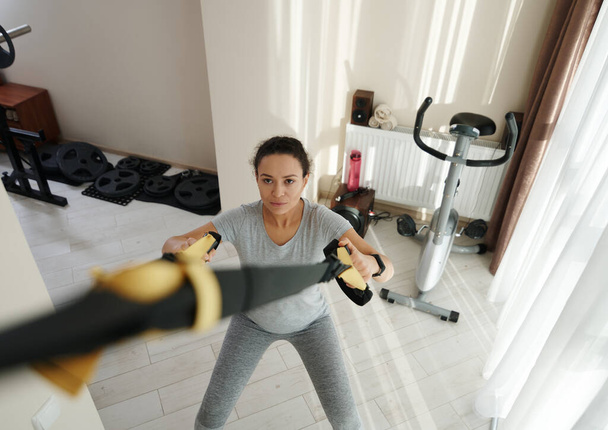 Hochwinkelaufnahme einer athletischen Frau, die zu Hause mit Fitnessbändern trainiert. Heimtrainingskonzept - Foto, Bild