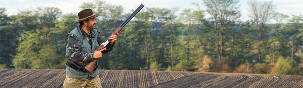 Metsästäjä ase kädessään metsästys vaatteita syksyllä metsässä etsimään pokaalin. Mies seisoo aseiden ja metsästyskoirien kanssa jäljittämässä peliä.. - Valokuva, kuva