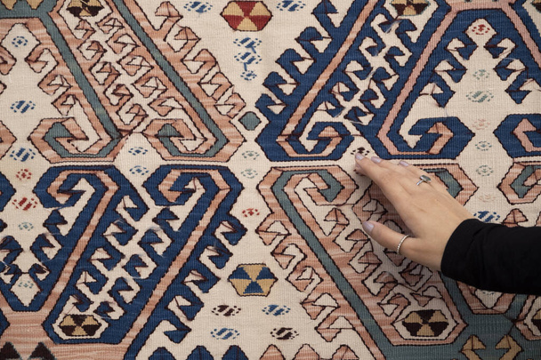 Vrouw in zwarte kleding raakt traditionele rug.Kleurrijke tapijten met etnische patronen in de tapijtwinkel. - Foto, afbeelding
