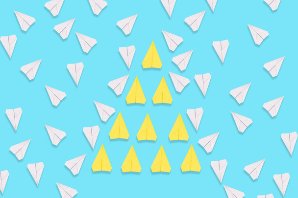 A group of yellow paper airplanes purposefully flies among the white planes. Blue background. Flat lay. The concept of leadership and teamwork. - Photo, Image