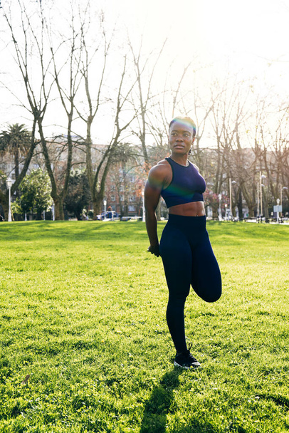 nero afro ragazza fare gamba si estende prima di andare per un corsa in un pubblico parco a tramonto - Foto, immagini