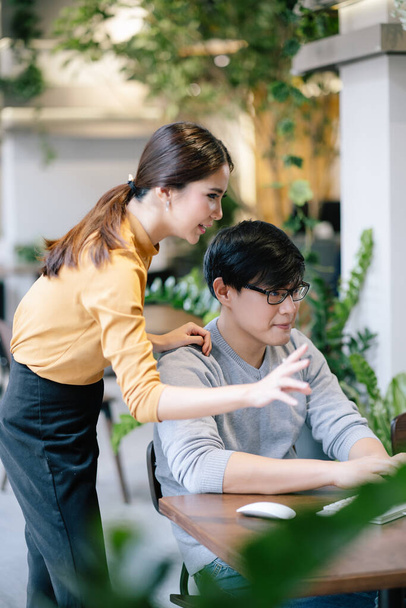 Deux collègues créatifs asiatiques en tenue décontractée intelligente discutent de nouvelles idées en utilisant un ordinateur PC dans un bureau modren, un espace de co-travail. Concept de travail d'équipe. - Photo, image