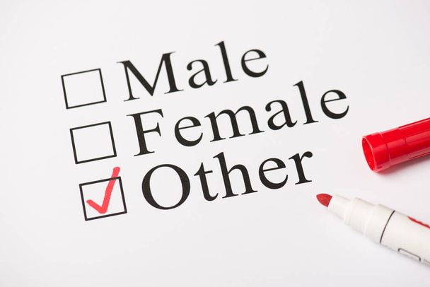 Foto superior de marcador de color rojo y papel con texto masculino femenino y otro aislado sobre el fondo blanco - Foto, imagen