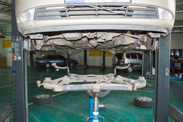 The front subframe removed from the vehicle rests on the hydraulic transmission rack. The car is hung on the lift in the car repair shop. - Photo, Image