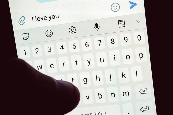Osoba trzyma telefon komórkowy i pisze wiadomość, że cię kocham. Zbliżenie ekranu klawiatury mobilnej w rękach osoby - Zdjęcie, obraz