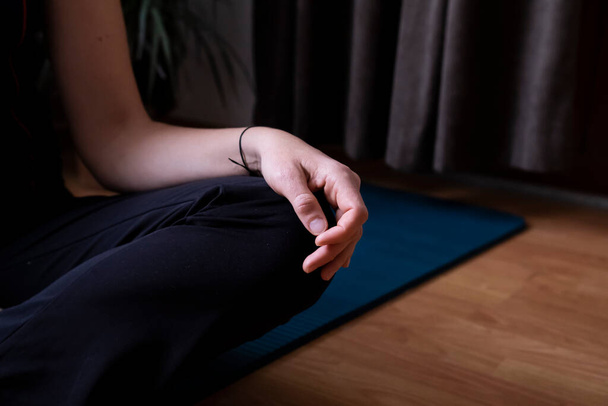 Kobieta siedząca na niebieskiej macie przygotowuje się do jogi. Kobieca ręka, pozycja lotosu. - Zdjęcie, obraz