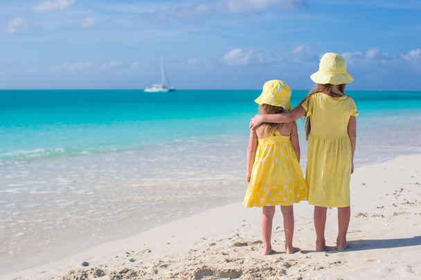 Вид ззаду на дві маленькі милі дівчата, які дивляться на море на білому пляжі
 - Фото, зображення