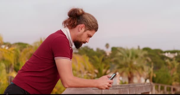 Sivunäkymä kaveri nojaa kaiteeseen, kun käytät matkapuhelin - Materiaali, video