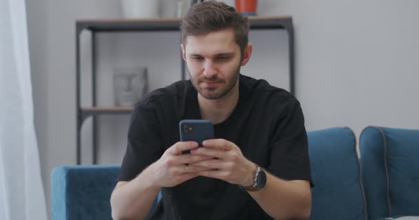 ενήλικος άντρας σερφάρει στο διαδίκτυο από smartphone στο σπίτι, πληκτρολογώντας μηνύματα σε chat ή παίζοντας βιντεοπαιχνίδια σε εφαρμογή - Πλάνα, βίντεο
