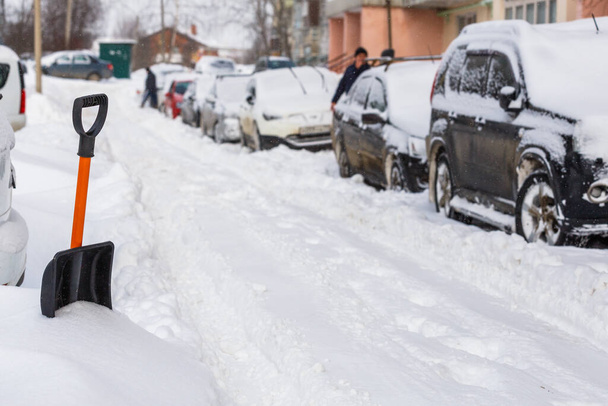 Маленькая пластиковая снежная лопата возле заснеженных машин в солнечное зимнее утро - Фото, изображение