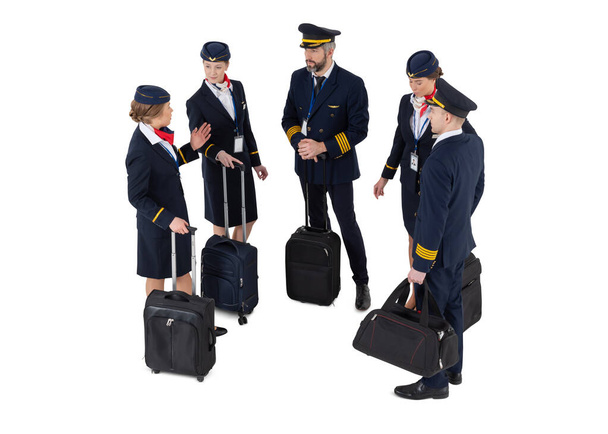 Κάτοψη ιπτάμενου πληρώματος με τις ταξιδιωτικές τσάντες και τις βαλίτσες του όρθιες και μιλώντας απομονωμένες σε λευκό φόντο - Φωτογραφία, εικόνα