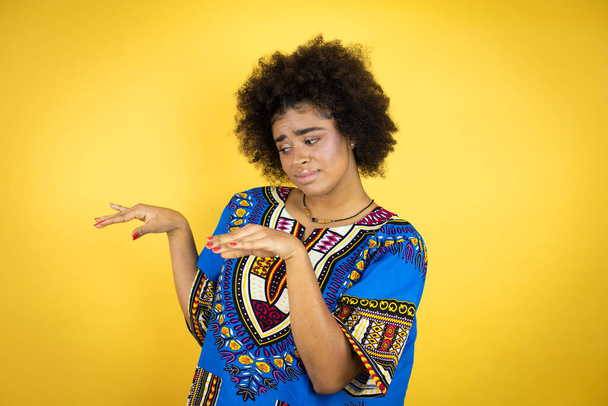 黄色の背景にアフリカの服を着ているアフリカ系アメリカ人の女性は嫌悪反応のために嫌悪感の表情、不満と恐怖を行う嫌悪感の顔。どんなコンセプトでも - 写真・画像
