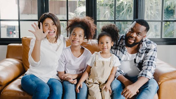 Happy African American family dad, mom and daughter having fun cuddle and video call on laptop on sofa at house. Self-isolation, stay at home, social distancing, quarantine for coronavirus prevention. - 写真・画像