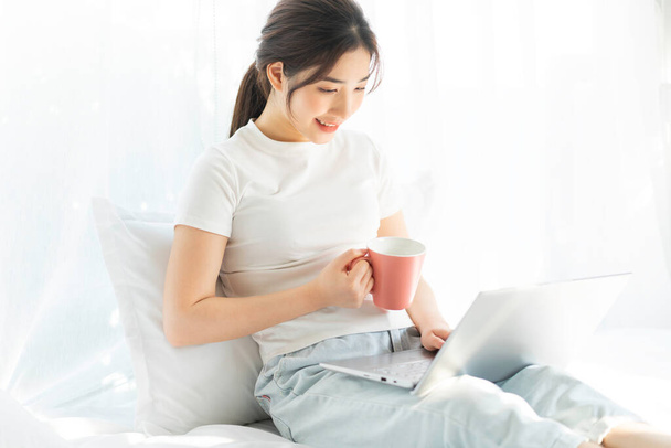jonge aziatische vrouw zitten op bed werken kijken home entertainment - Foto, afbeelding