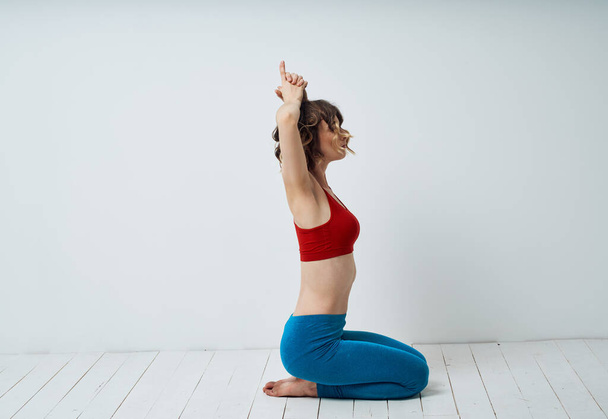 Una esbelta mujer muestra ejercicios de yoga en una habitación luminosa, sentada en el suelo con los brazos levantados - Foto, imagen