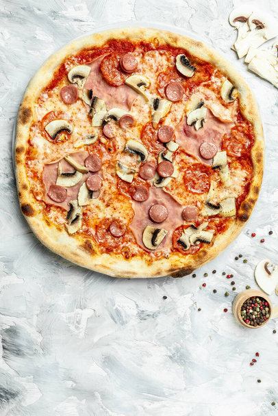 Italian pizza is cooked in a wood-fired oven. Capriciosa pizza. Classic pizza with ham and mushrooms on a light background, top view. - Photo, Image