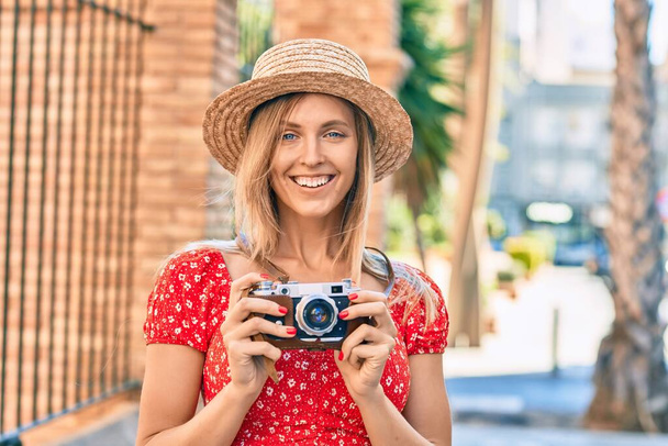Młoda blondynka turystka nosi letni styl używając zabytkowej kamery w mieście. - Zdjęcie, obraz