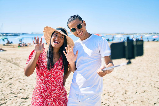 Giovane coppia latina sorridente felice facendo selfie dallo smartphone in spiaggia. - Foto, immagini