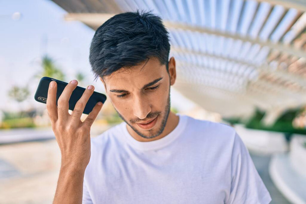 Giovane uomo latino sorridente felice ascolto messaggio audio utilizzando smartphone in città. - Foto, immagini