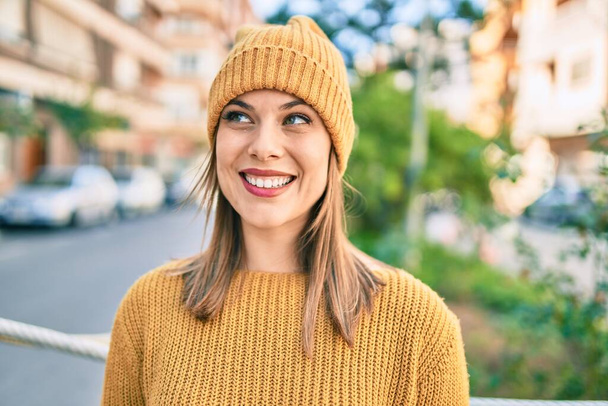 Kış tarzı giyinen genç sarışın kadın şehirde mutlu bir şekilde gülümsüyor.. - Fotoğraf, Görsel