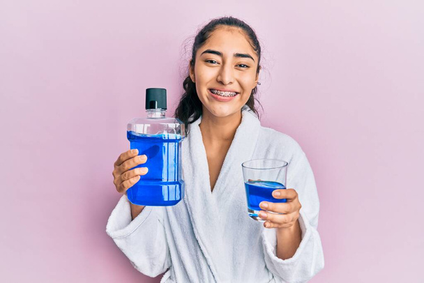 Hispanic teenager girl with dental braces holding mouthwash smiling with a happy and cool smile on face. showing teeth.  - Photo, Image