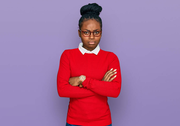 Молодая африканская американка в повседневной одежде и очках скептически и нервно, с неодобрительным выражением лица со скрещенными руками. отрицательный человек.  - Фото, изображение