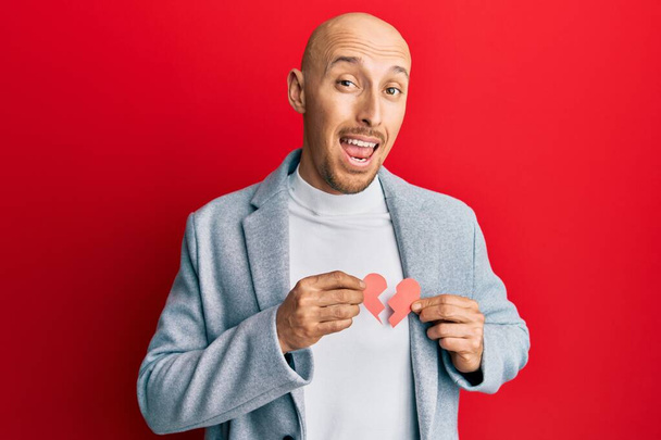 Bald man with beard holding broken heart paper shape celebrating crazy and amazed for success with open eyes screaming excited.  - Photo, Image