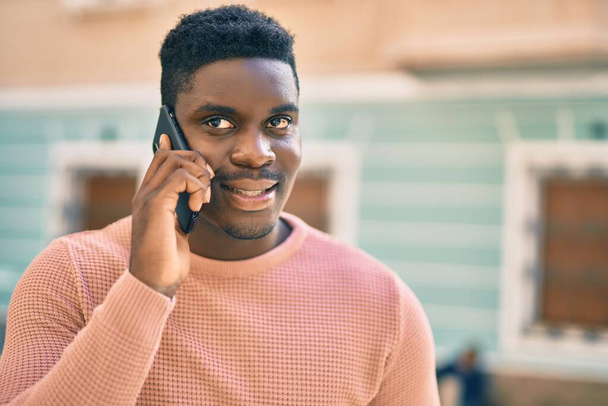 Giovane uomo afroamericano sorridente felice parlando sullo smartphone in città. - Foto, immagini