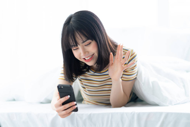 Mulher asiática bonita usando telefone na cama no quarto - Foto, Imagem
