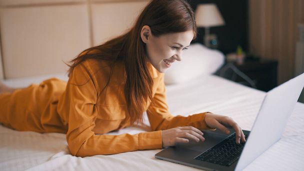 mujer se encuentra en la cama delante de la computadora portátil trabajo freelance internet - Foto, imagen