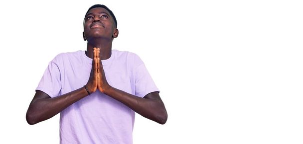 Joven afroamericano vestido con ropa casual mendigando y rezando con las manos junto con la esperanza de expresión en la cara muy emocional y preocupado. mendicidad.  - Foto, Imagen