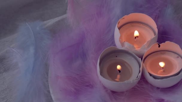 Composición de cáscara de huevo blanco con vela ardiente en el interior. Luz de la vela. Decoraciones de Pascua brillante con plumas de pájaro. Colores pastel. Humo de llama - Imágenes, Vídeo