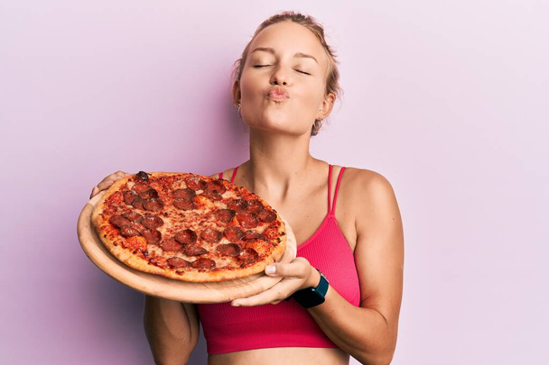 カメラを見ているイタリアのピザを持っている美しい白人女性は、キスが美しく、セクシーであることを吹く。愛の表現.  - 写真・画像