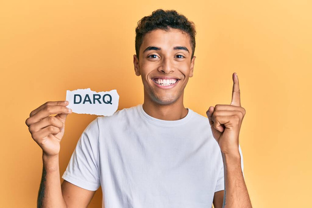 Young handsome african american man holding darq technologies word smiling with an idea or question pointing finger with happy face, number one  - Photo, Image