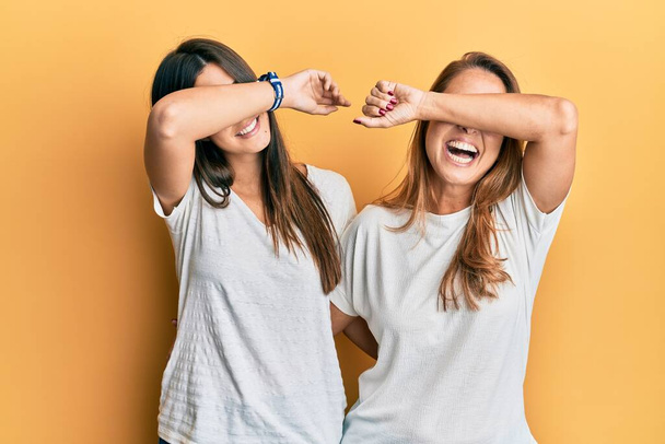 Família hispânica de mãe e filha vestindo camiseta branca casual sorrindo alegre jogando peek um boo com as mãos mostrando rosto. surpreso e saiu  - Foto, Imagem
