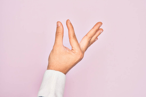 Hand of caucasian young man showing fingers over isolated pink background picking and taking invisible thing, holding object with fingers showing space - 写真・画像