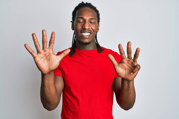 Africký Američan s copánky na sobě ležérní oblečení ukazuje a ukazuje s prsty číslo devět a zároveň se usmívá sebevědomě a šťastně.  - Fotografie, Obrázek