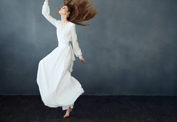 Woman in long white dress on gray background dance model emotions - Фото, изображение