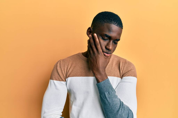 Genç, Afro-Amerikalı bir adam günlük kıyafetler giyip kollarını kavuşturup depresyondan sıkılmış ve yorgun görünüyor..  - Fotoğraf, Görsel