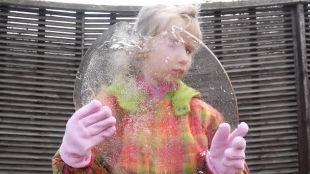 Een meisje onderzoekt scheuren in een stuk doorzichtig ijs dat ze in haar handen houdt.. - Video